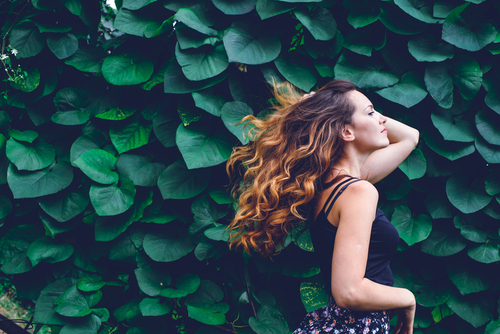 Aveda model with hair in the wind in front of a wall of ivy leaves
