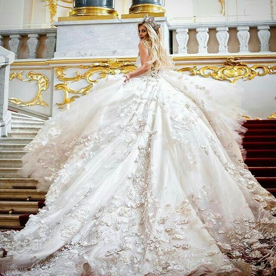 woman looks over her shoulder as she climbs a staircase in a ball gown