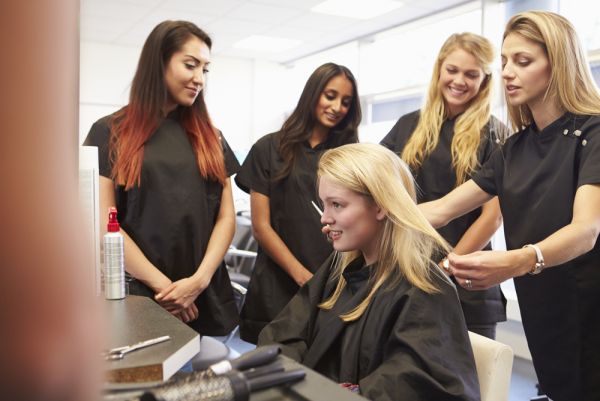 Cosmetology students together working on a blonde woman's hair