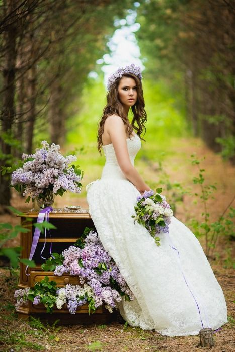 woman in a wedding gown sits outdoors with lilac bouquet