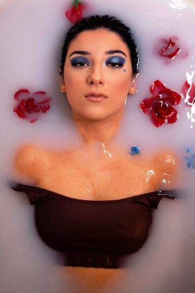 woman with blue eyeshadow in tub with floating flowers